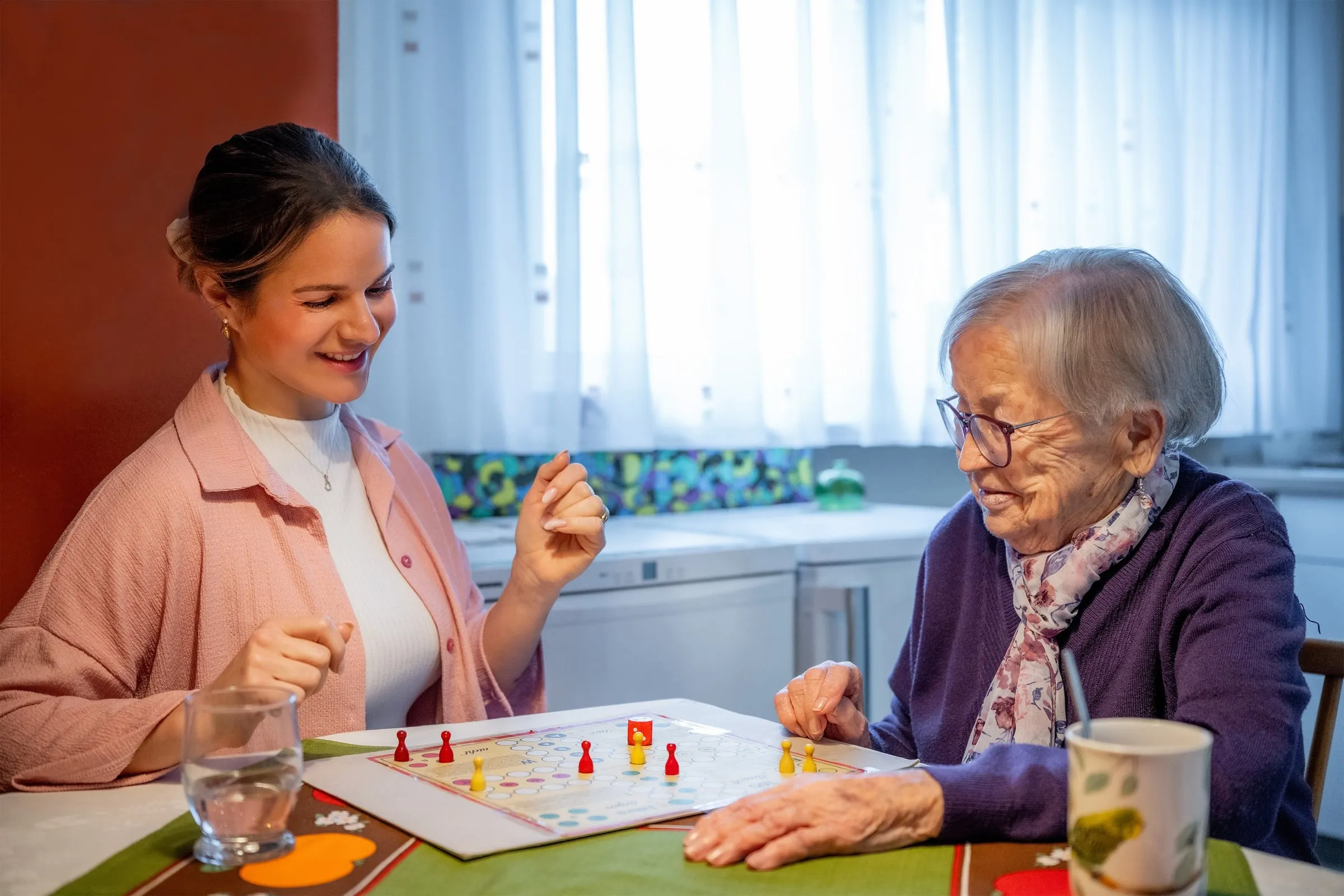 Eine ältere Frau und eine Begleiterin spielen gemeinsam am Tisch.